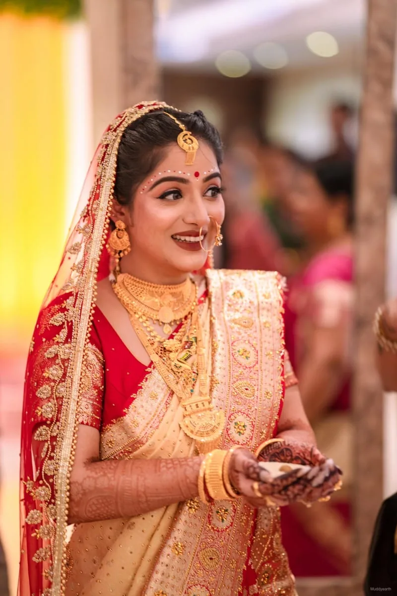 Bridal makeup Odisha by Romma — bride in red and cream saree holding ceremonial bowl